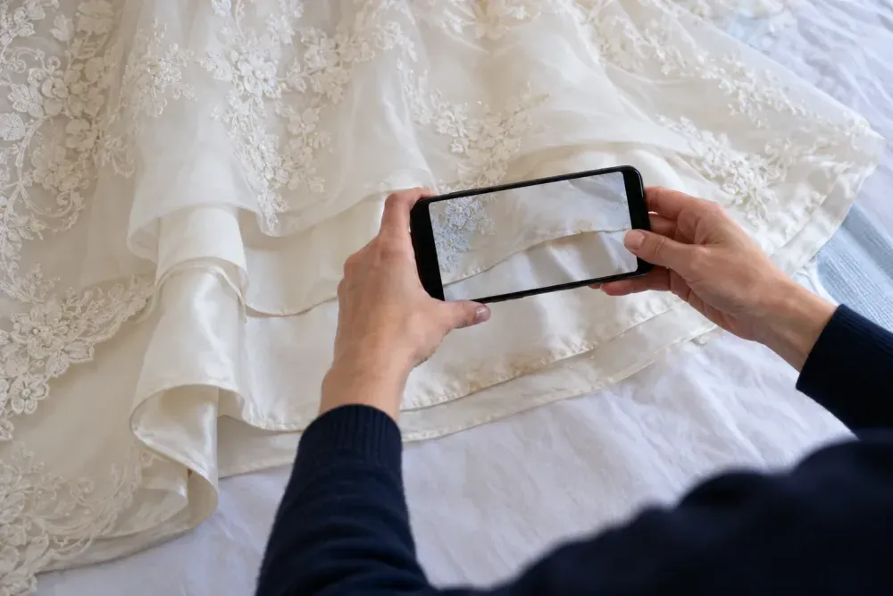 A person photographing marks on a wedding dress hem with a smartphone before cleaning.